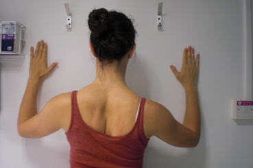 Photo of patient standing with palms placed flat on wall.