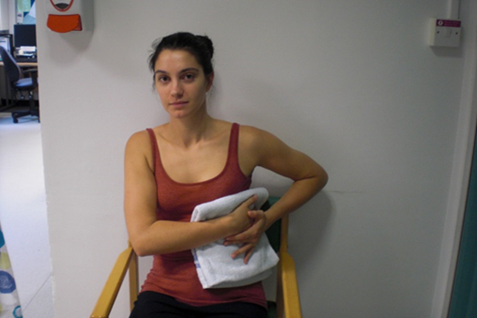 Patient seated holding a folded towel pad against their side.