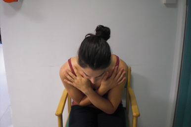 Photo of a seated patient in the same arms folded position with their torso bent forwards.