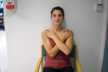 Photo of seated patient with arms folded across chest and hands palms down on front of shoulder.
