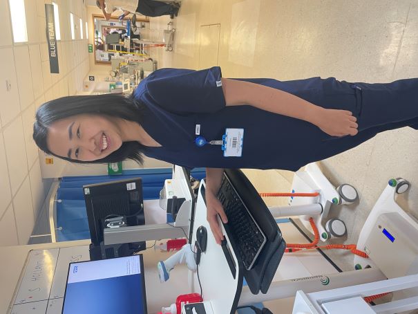 Photo of doctor in scrubs standing at a computer in a ward