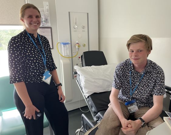 Photo of a doctor standing at a bedside with a volunteer 'patient' seated on bed