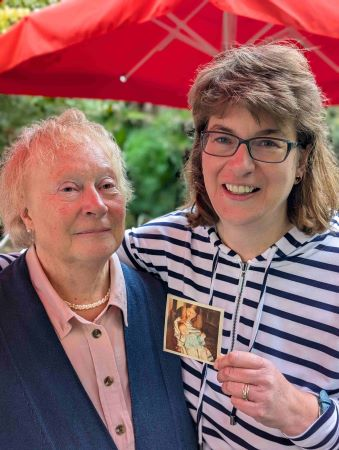 an older and younger woman arm in arm holding an old photo of mother and baby